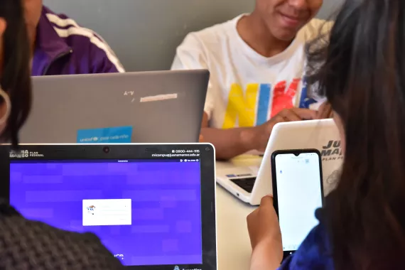 J&oacute;venes en una clase con dispositivos m&oacute;viles y computadoras