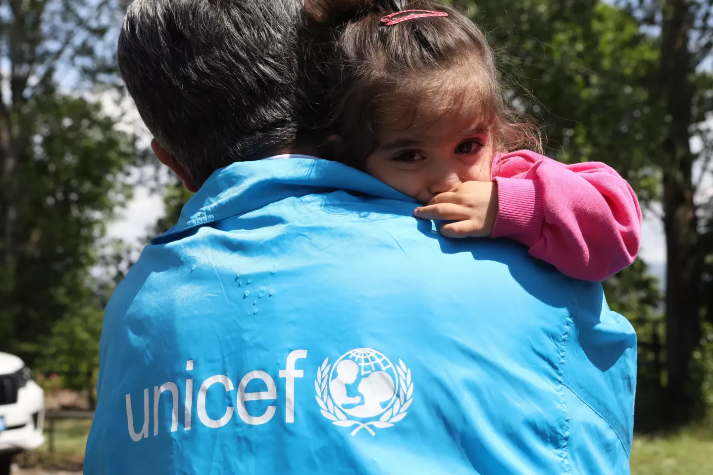 A toddler is resting her head on unicef employee's shoulder