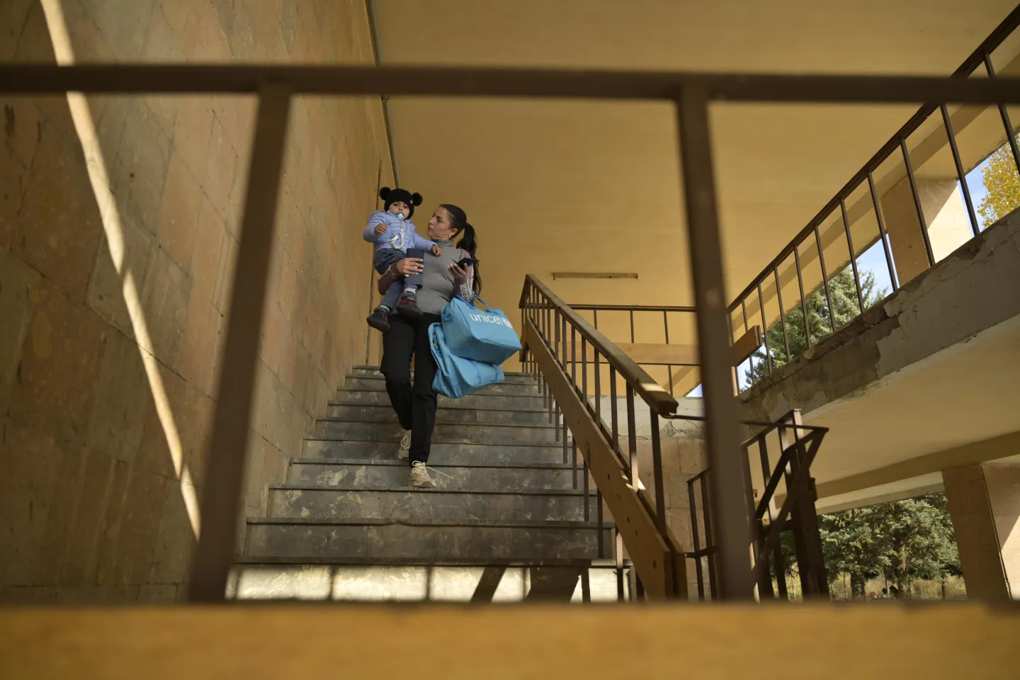 A mother is going down the stairs holding two big bags. 