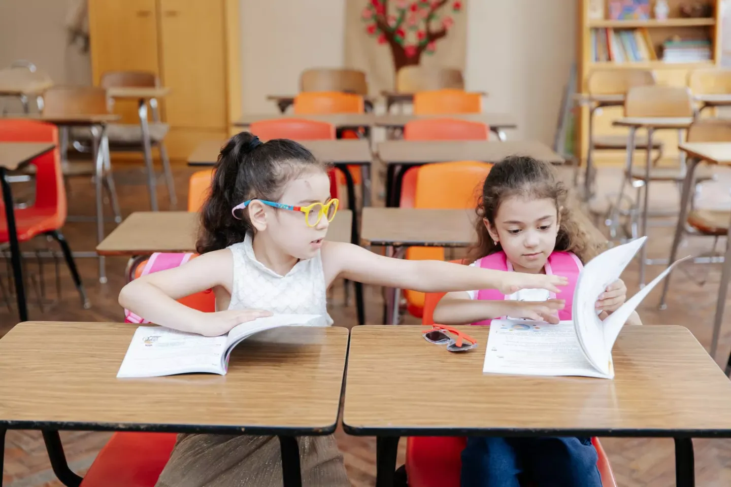 Two girls sitting on the desk in the classroom. 