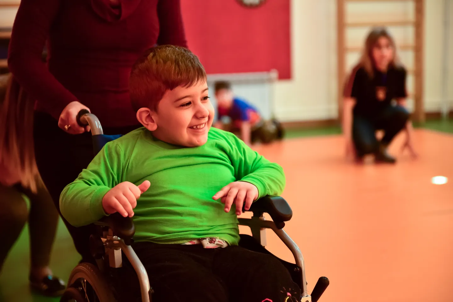 Հաշմանդամություն ունեցող և սայլակով տեղաշարժվող տղան մասնակցում է ֆիզկուլտուրայի դասընթացին և շատ ուրախ է. նա ժպտում է: 