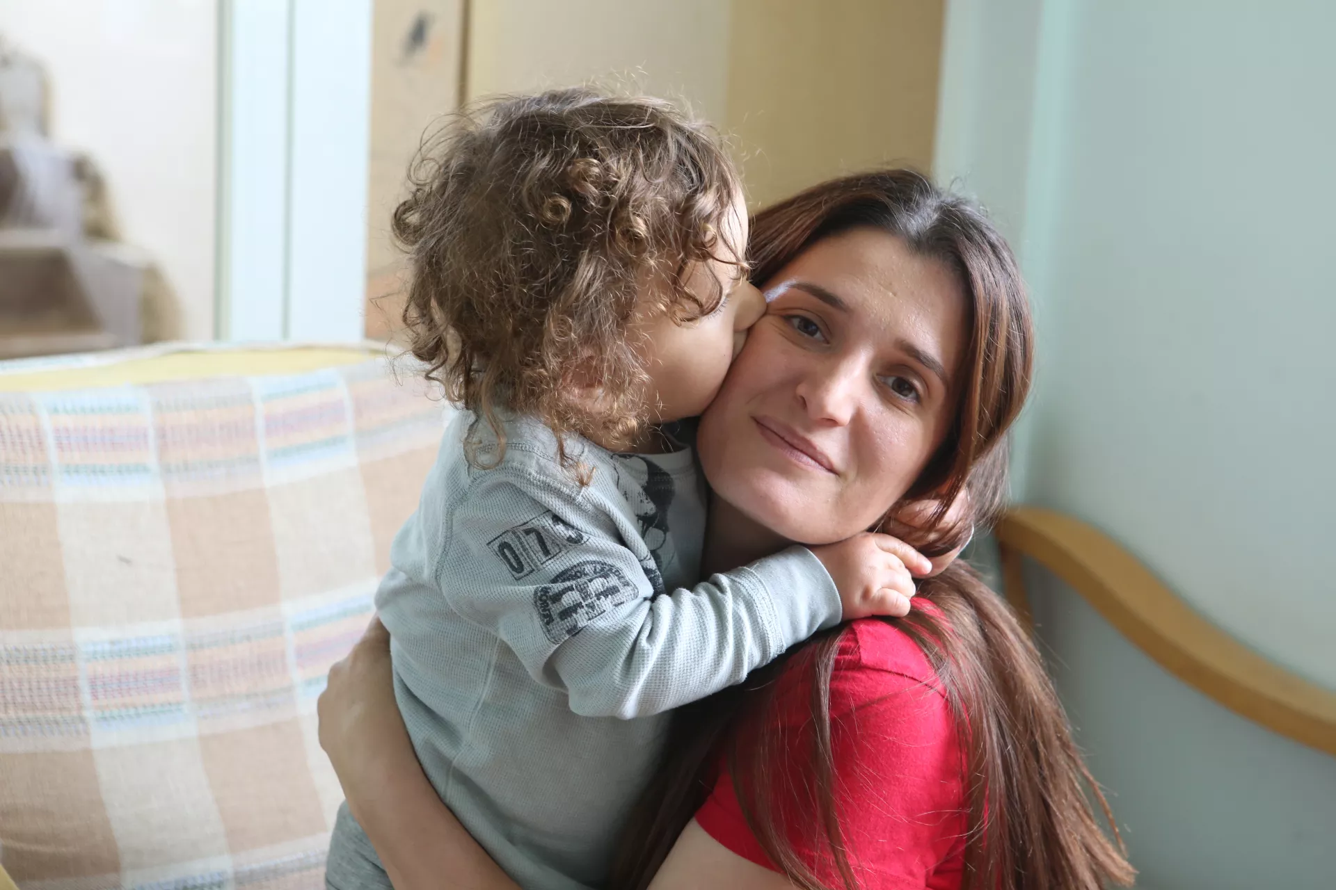 Toddler kissing his mother who is posing for the camera