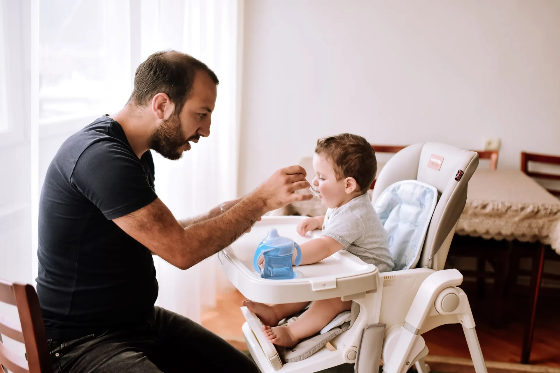 Father feeding his toddler, who is sitting on a highchair