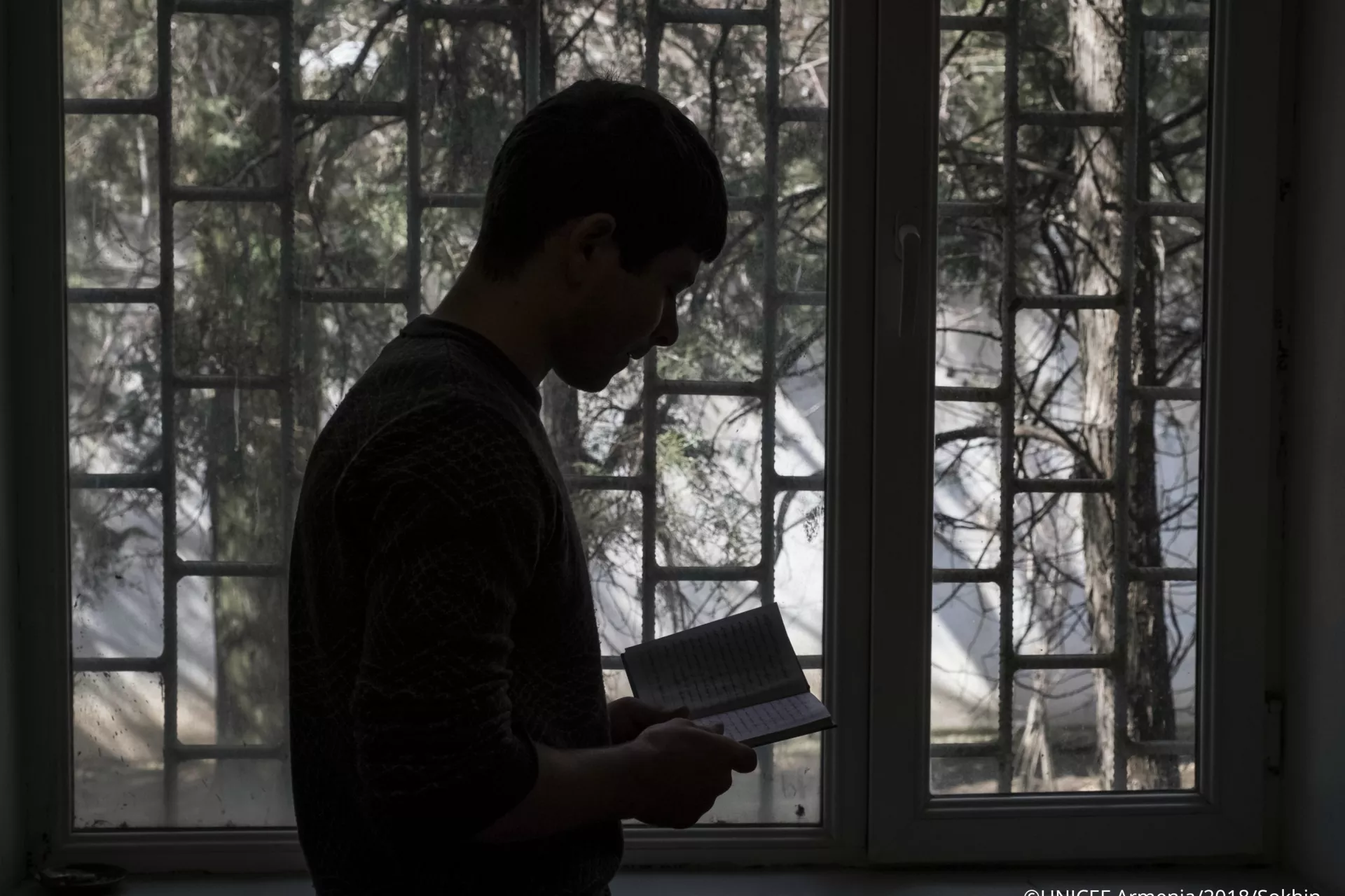 A 17-year old boy reading poems by a window in a room of "Noubarashen" penitentiary institution for adolescents.