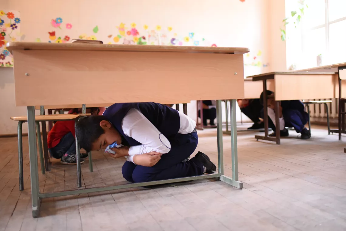 A boy hides under the table covering his mouth with peace of cloth during the preparedness drill in Nerqin Tsakhkavan village.