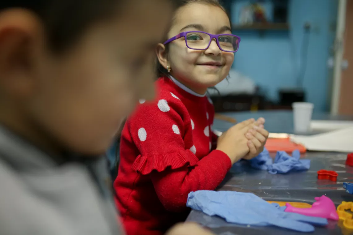 Girl is smiling to the camera while wrking with clay.