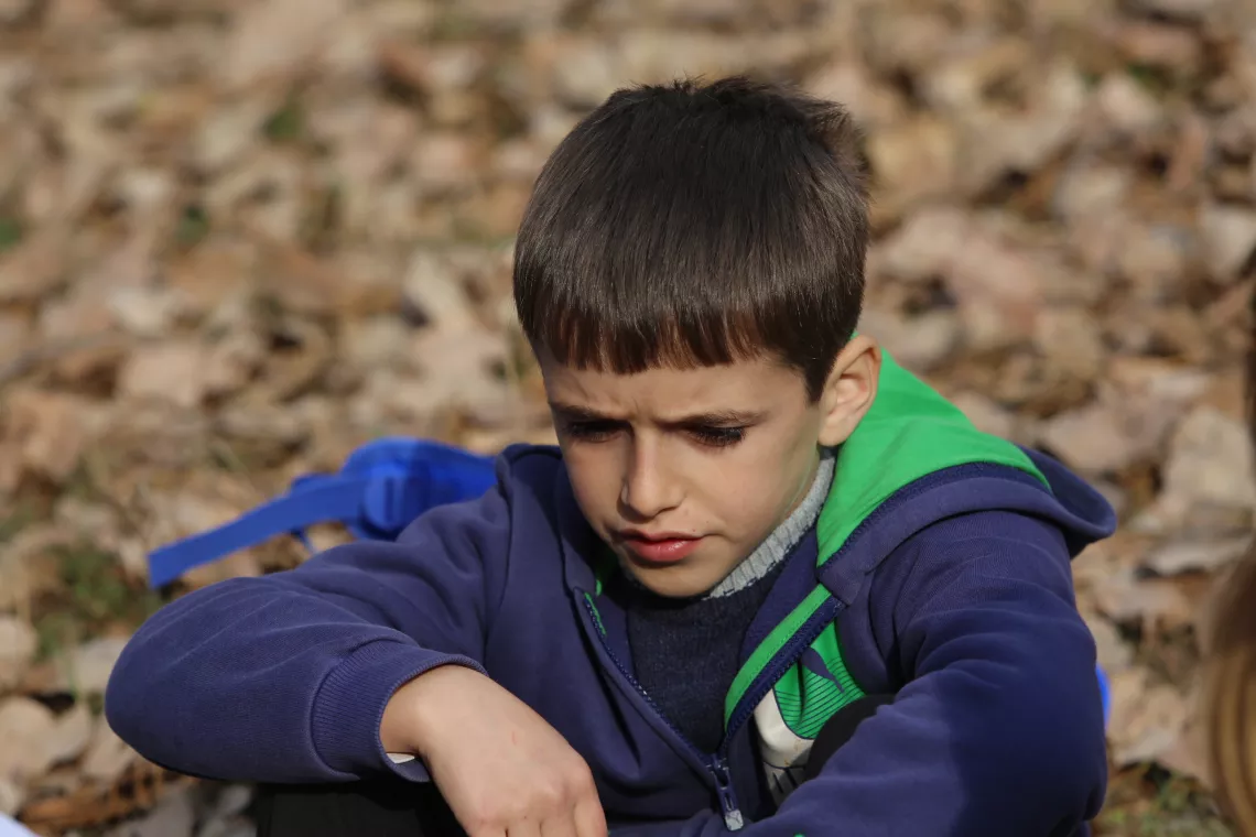 A schoolboy sitting on the ground, thinking.