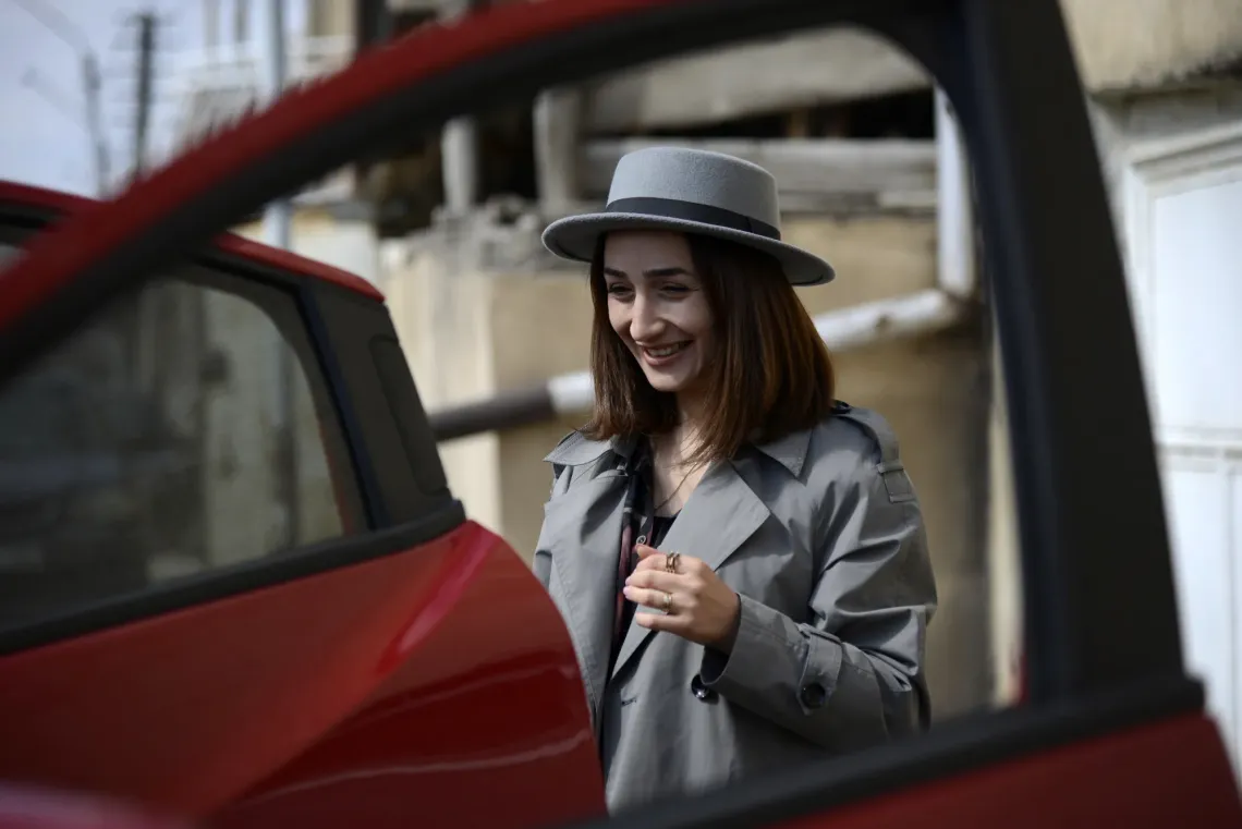 A woman is smiling standing next to red car