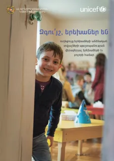 Տղան ժպտում է մանկապարտեզի իր սենյակի կիսաբաց դռնից: 