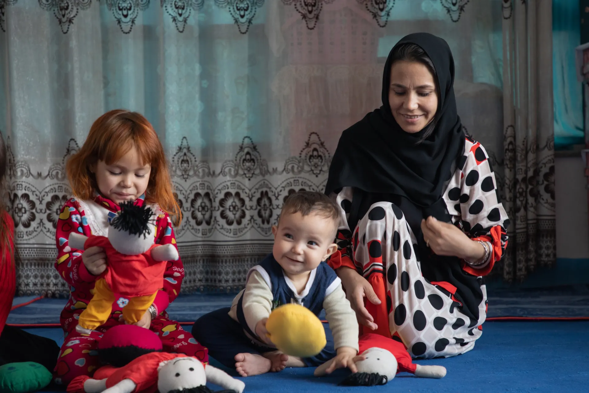 Little girls play with dolls while mother watches