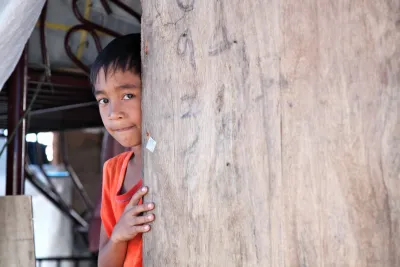 A boy looks out tentatively from behind a door