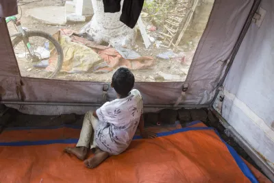 a boy sits alone looking out a tent window