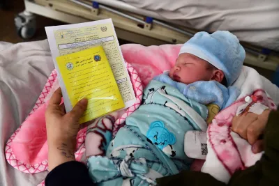 hand holding a birth certificate next to a sleeping newborn