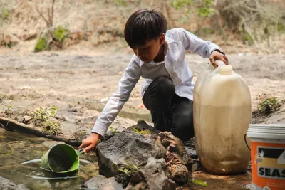 A boy scoops water from a stream into a jerry can