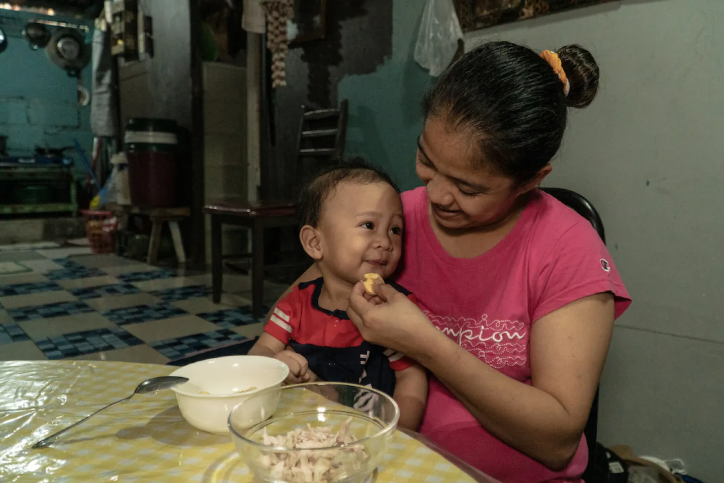A mother feeding her son as they both smile at each other