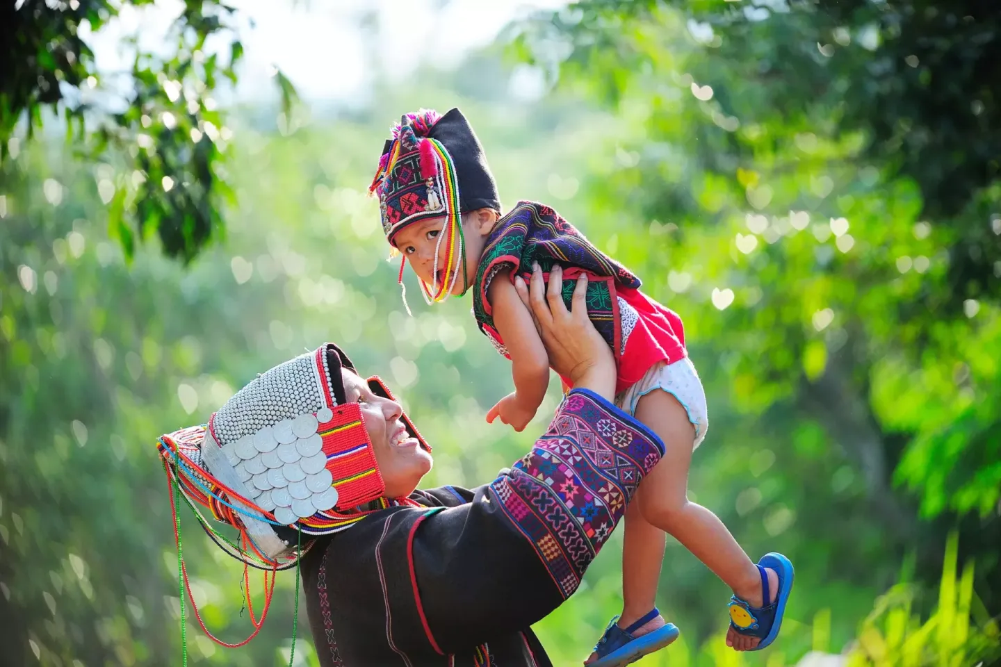 A mother holds her baby up. both are in traditional burmese clothing