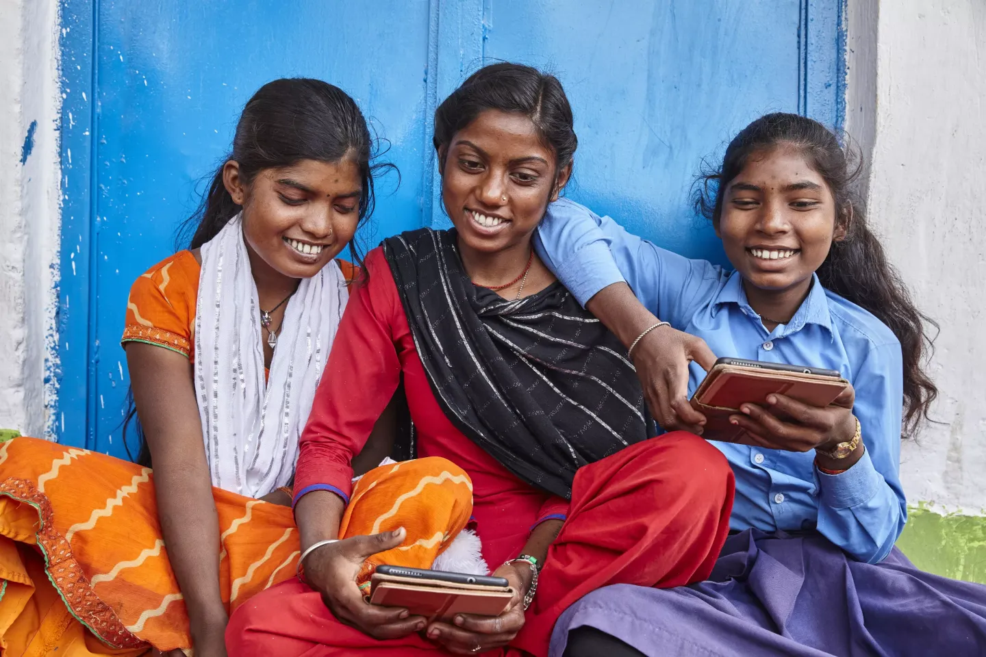 three girls sit against a sky blue wall