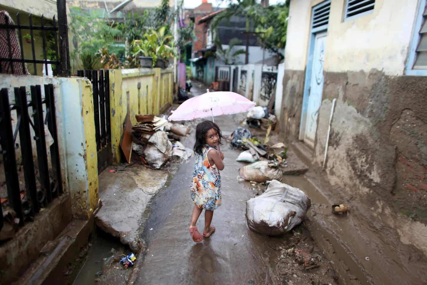 A small girl, carrying an umbrella in the rain, walks past large bags of garbage and other debris on a narrow street in the flood-affected Bukit Duri neighbourhood of Central Jakarta.
