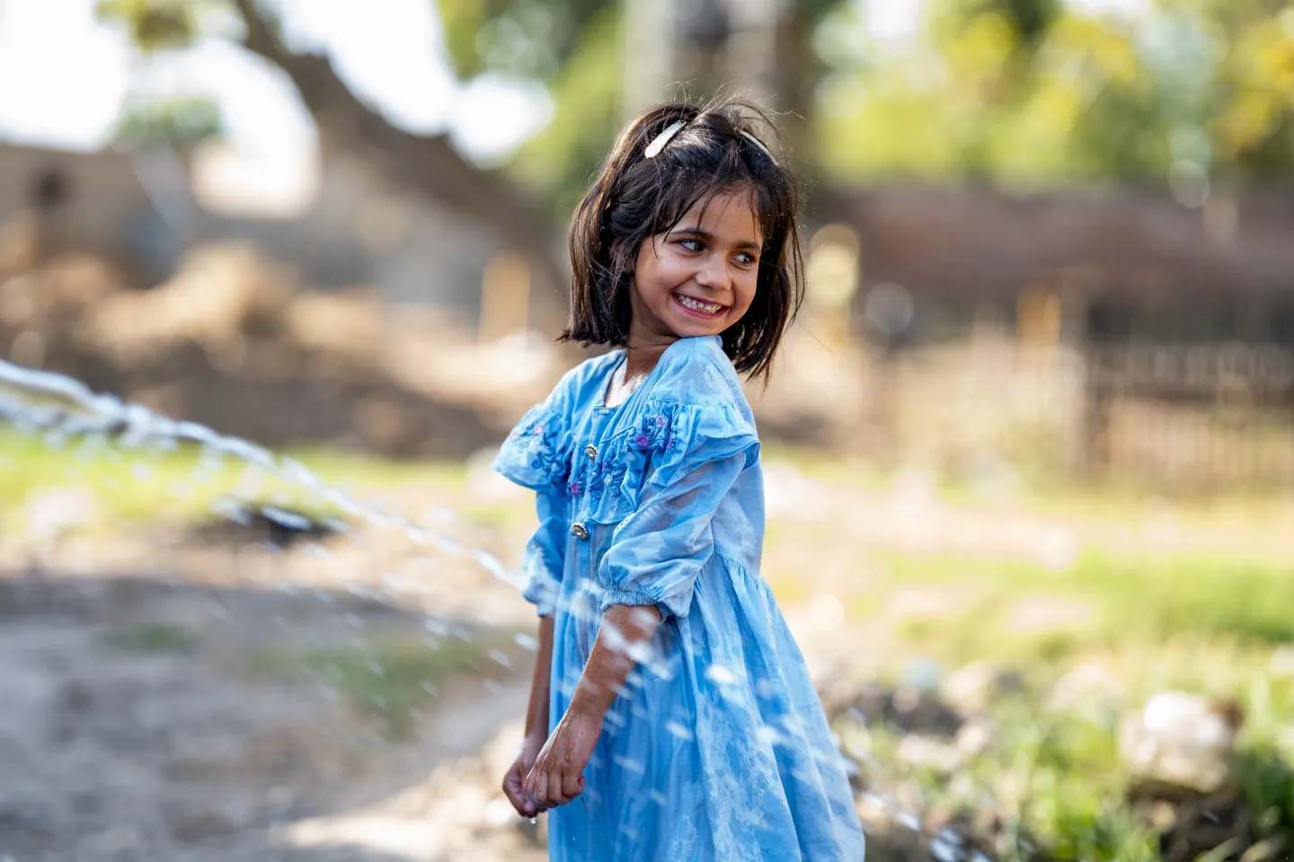 a girl in a blue dress smiles as she cools off in a spray of water