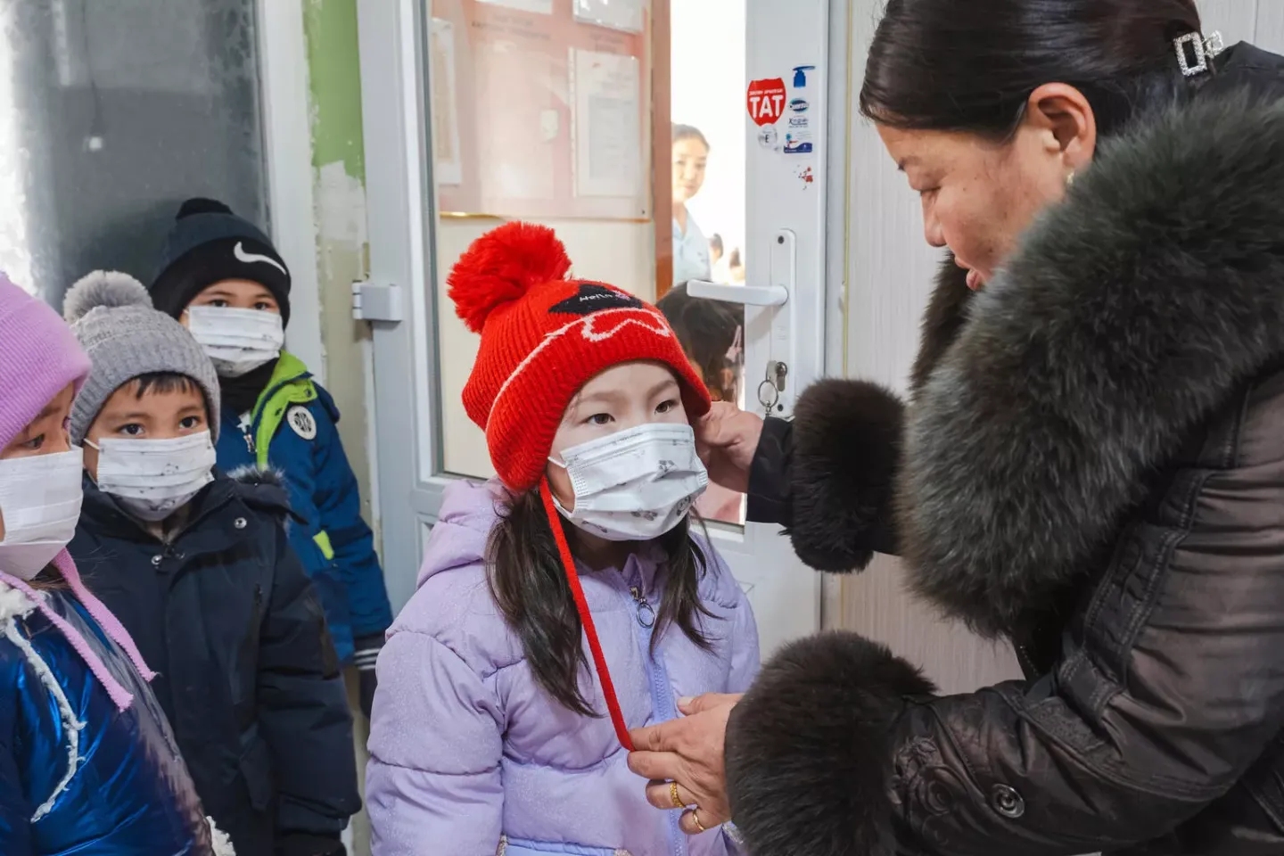 Kindergarten teacher Munkhtuya M. helps a child put on a face mask before outdoor activities in Nalaikh, Mongolia. 