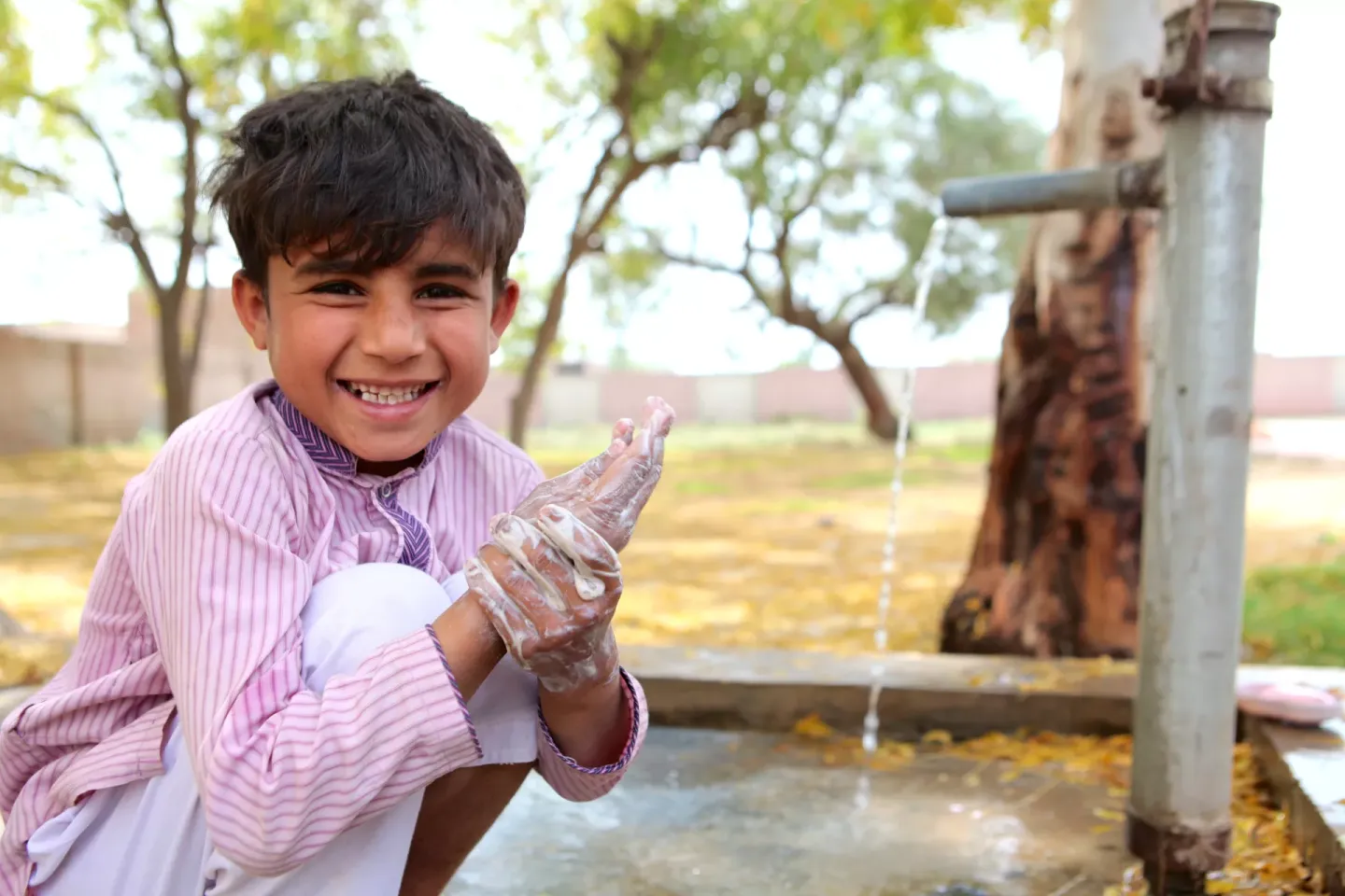 A boy washes his hands with soap at a sink
