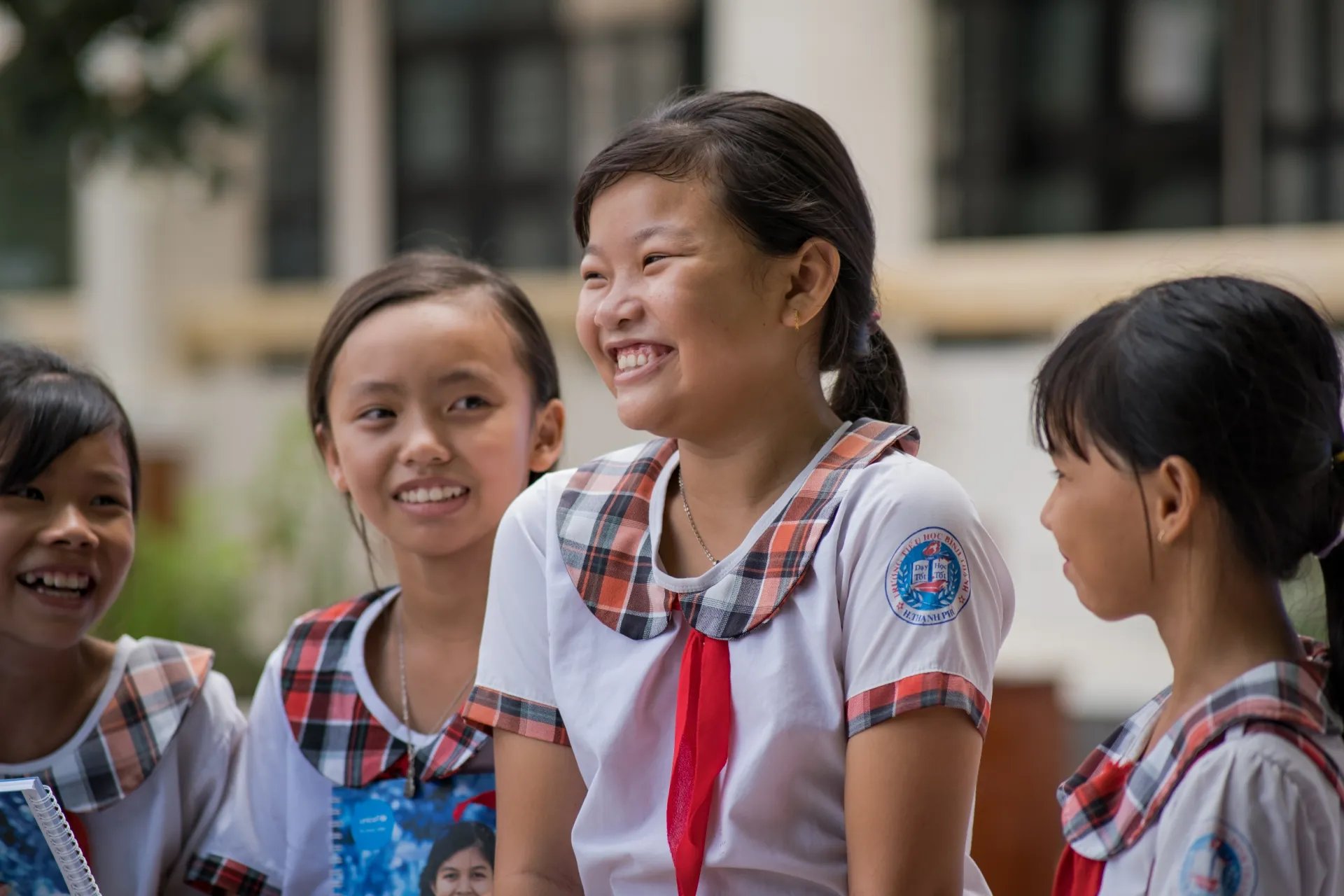 A girl in school uniform stands smiling with other students
