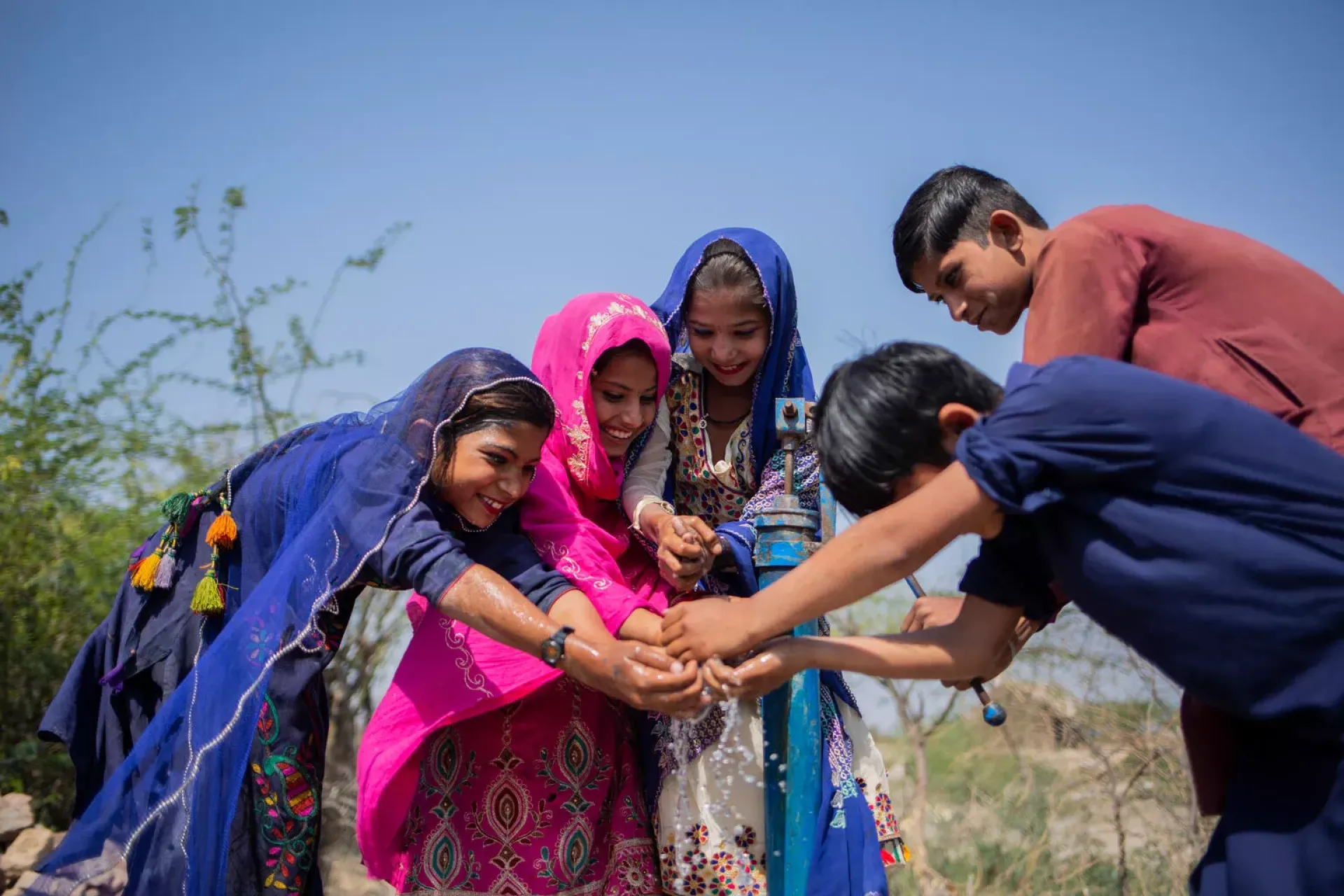 Three girls and two boys play with water from a hand-pump in Pakistan