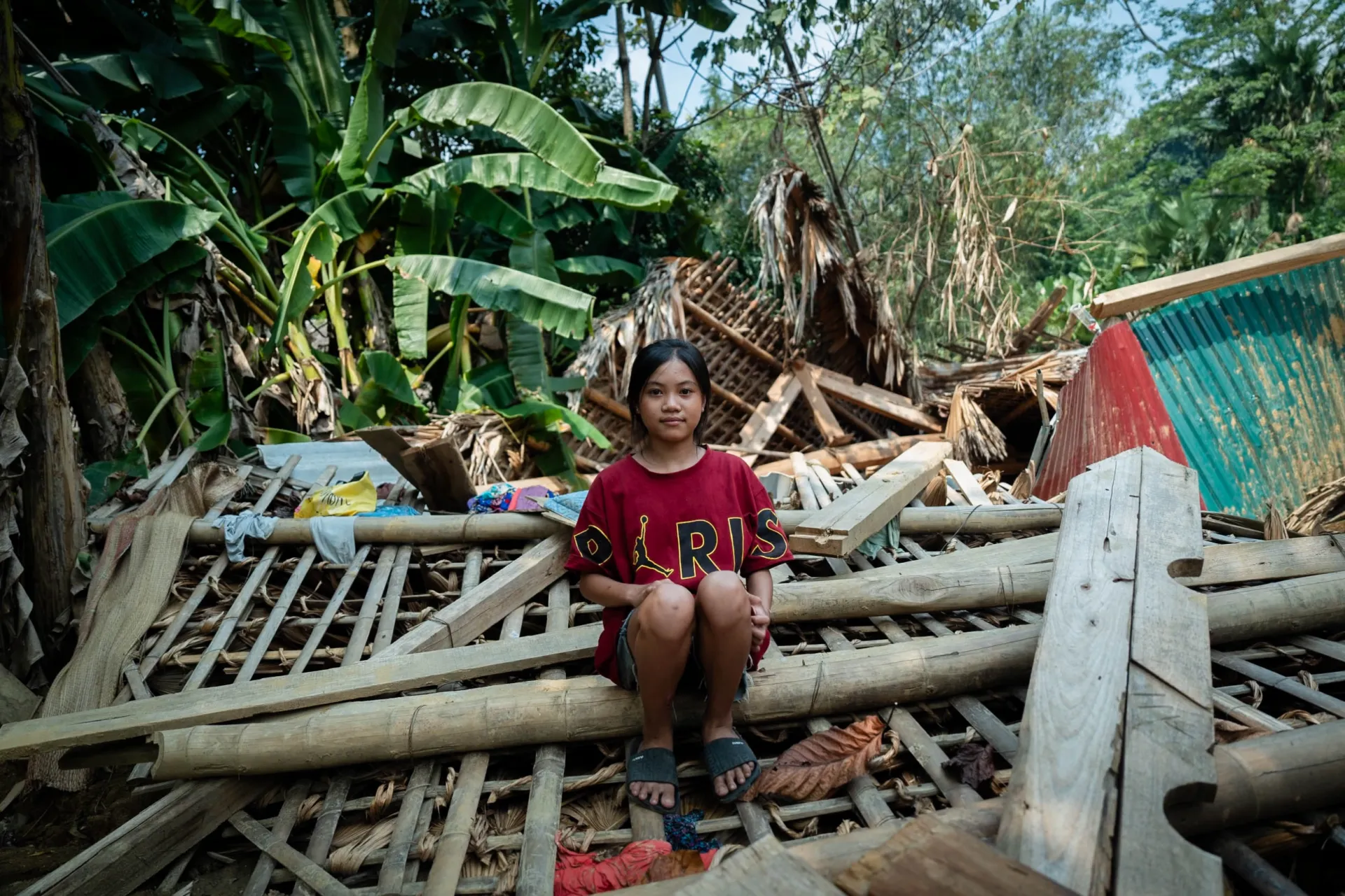 A girl sits on the demolished remains of her home