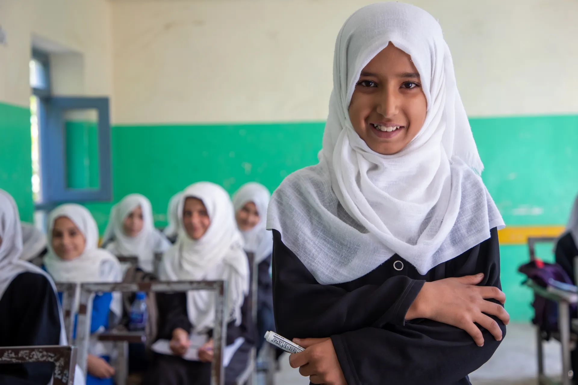 A 4th grader stands in her classroom with classmates behind her.