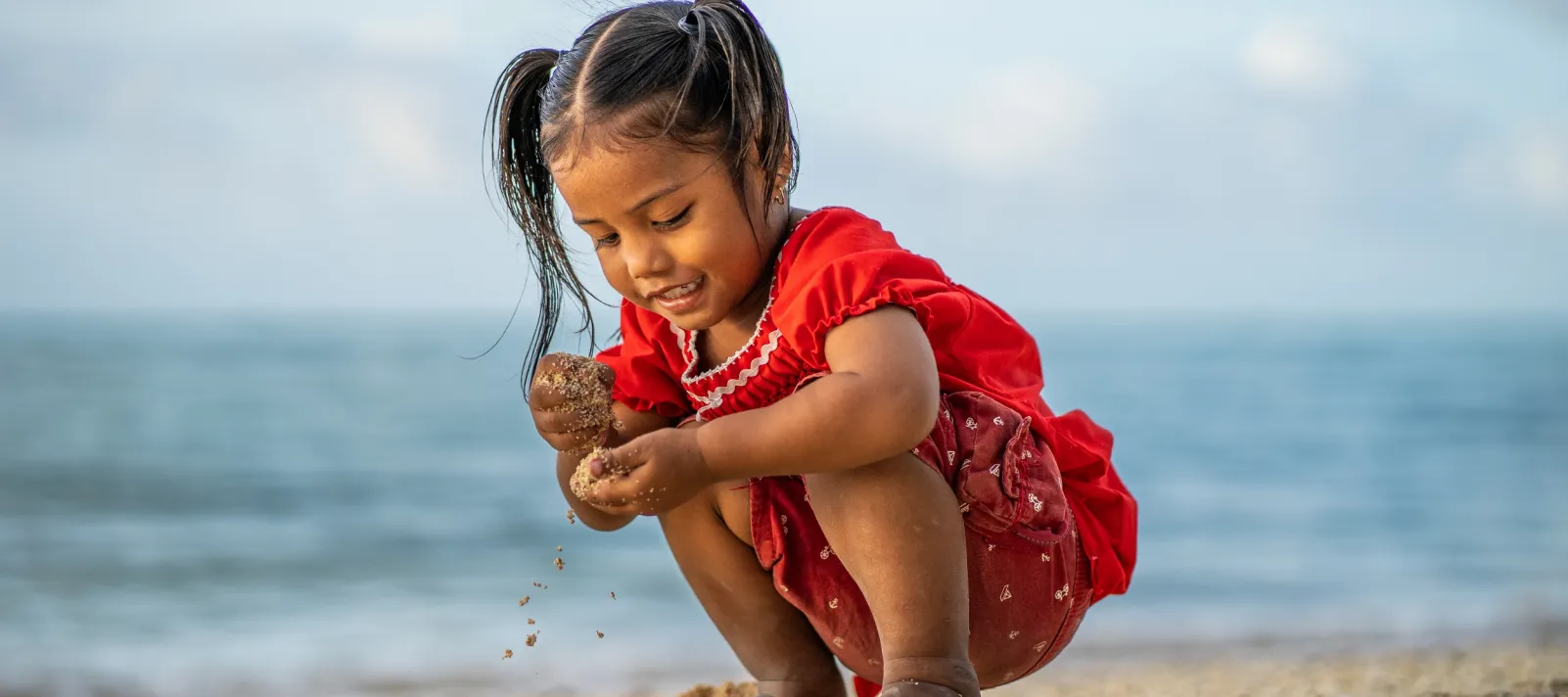 Small girl crouches to play in the sand seaside.