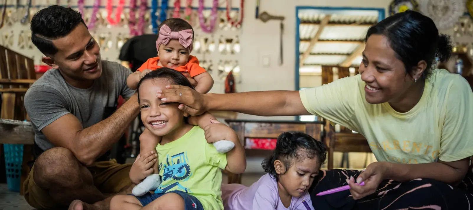 Parents play on the floor with their two toddlers and a baby.