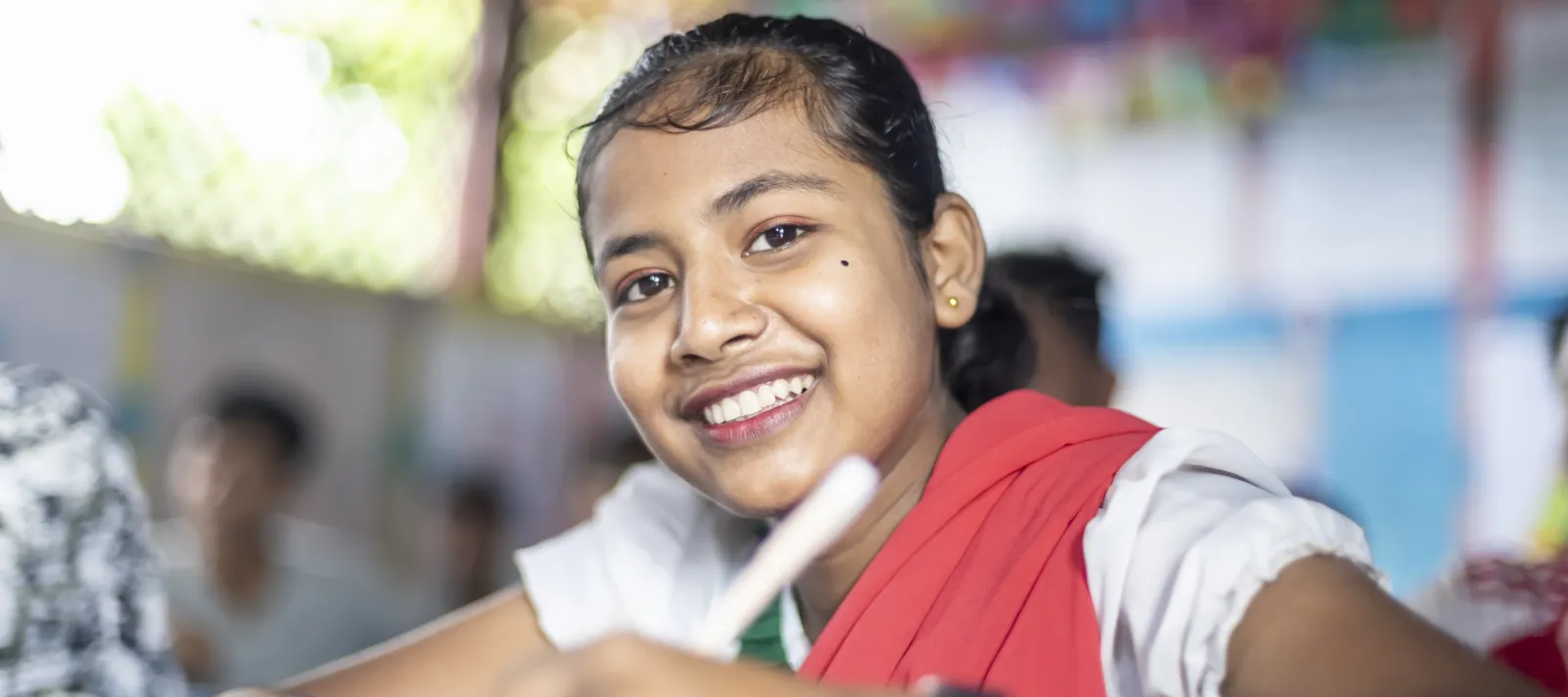 Smiling girl at a desk holding a pen.