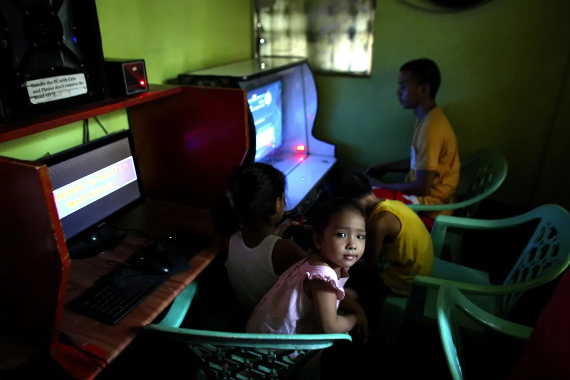 a girl sits beside young boys at computers playing video games in a darkened room inside an Internet caf&eacute; on the outskirts of Metropolitan Manila, Philippines.