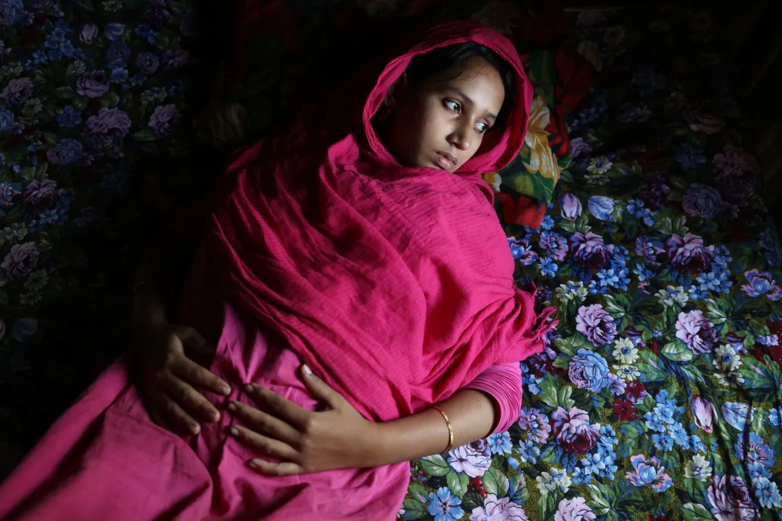 A pregnant teen girl in a magenta hijab lies on the floor.