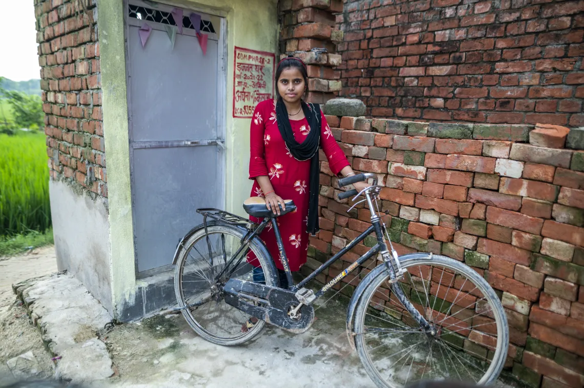 Aarti stands with her bicycle outside a toilet 