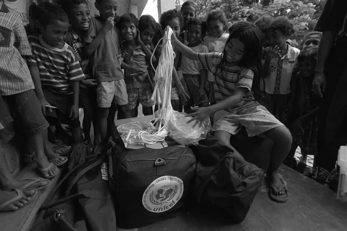  girl, surrounded by other children, smiles as she unpacks the contents of a UNICEF 'edukit'