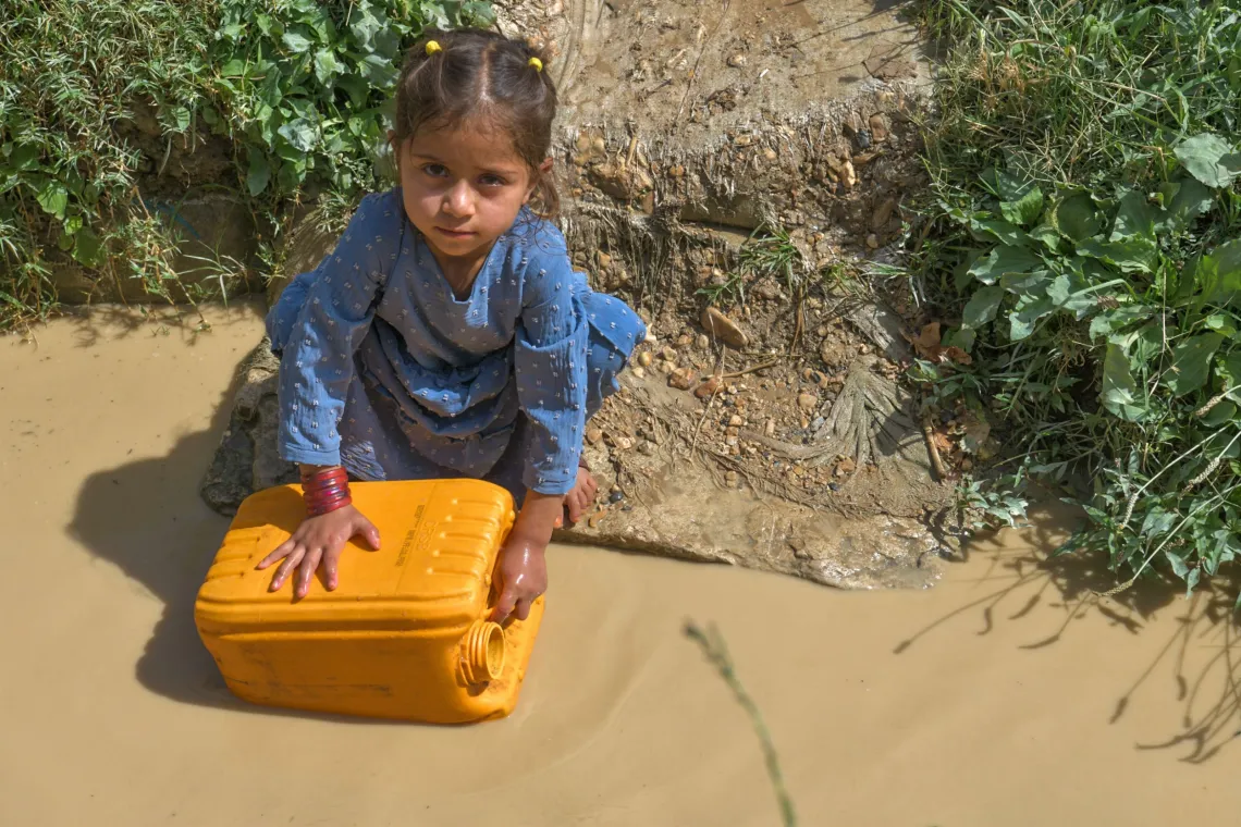 a little girl fills a jerry can at a muddy pool