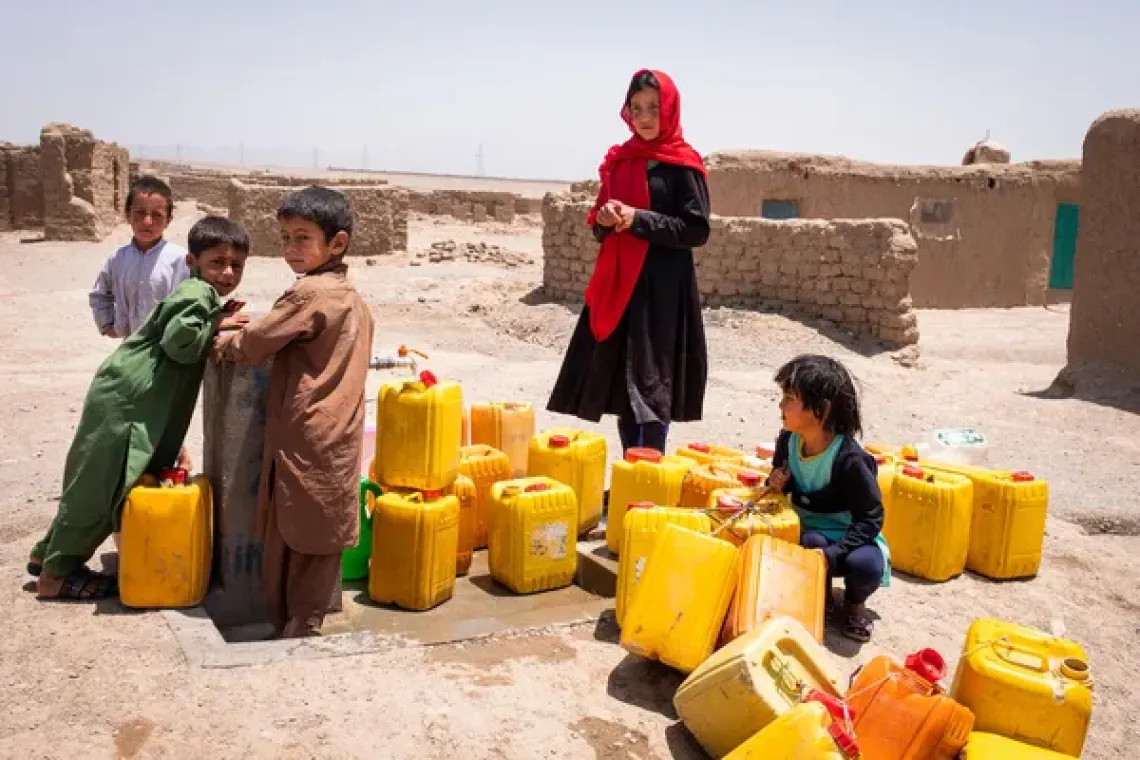 Children stand patiently awaiting the water pressure to rise and fill their jerrycans with clean water from a public pump.