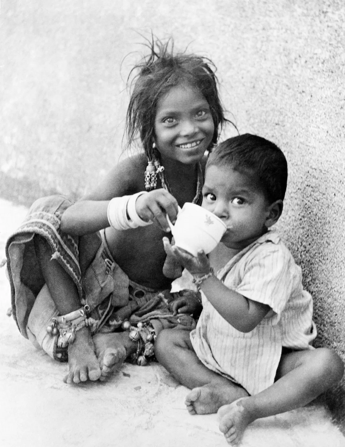a girl and her younger sibling share a cup of milk