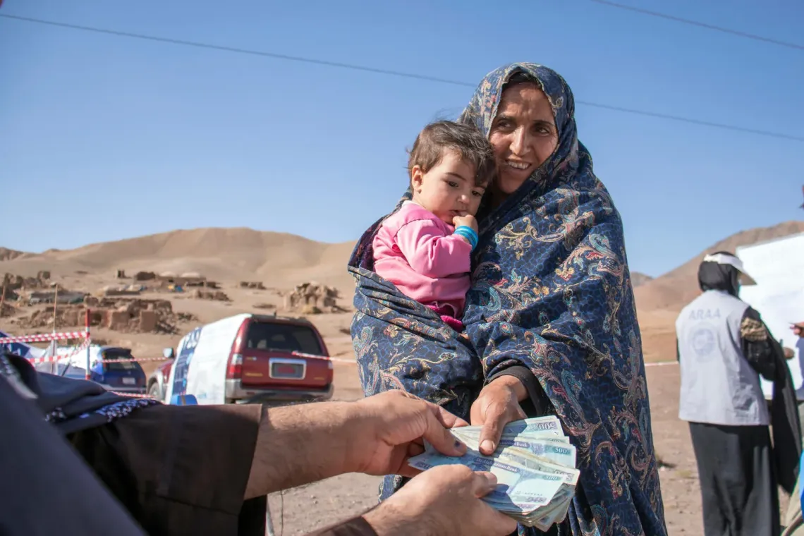 A woman holding her 10-month-old babyreceives cash assistance from a UNICEF programme.