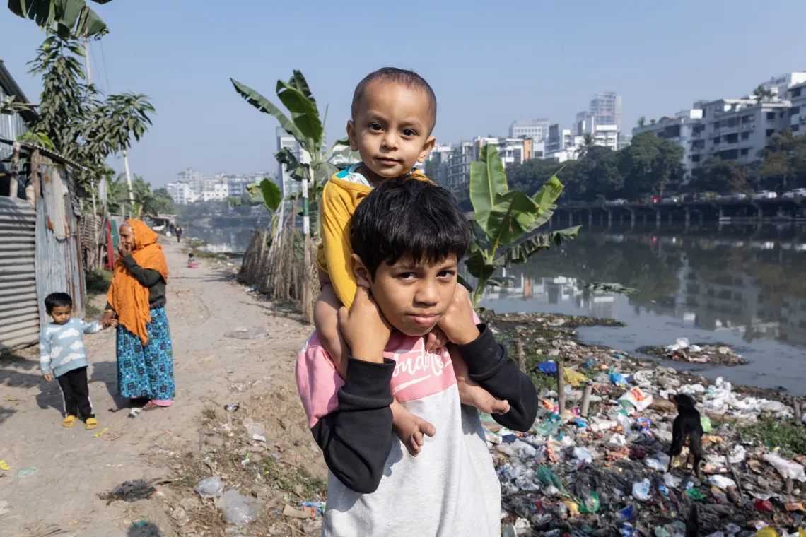 a boy with his little brother on his shoulders stands amid piles of trash
