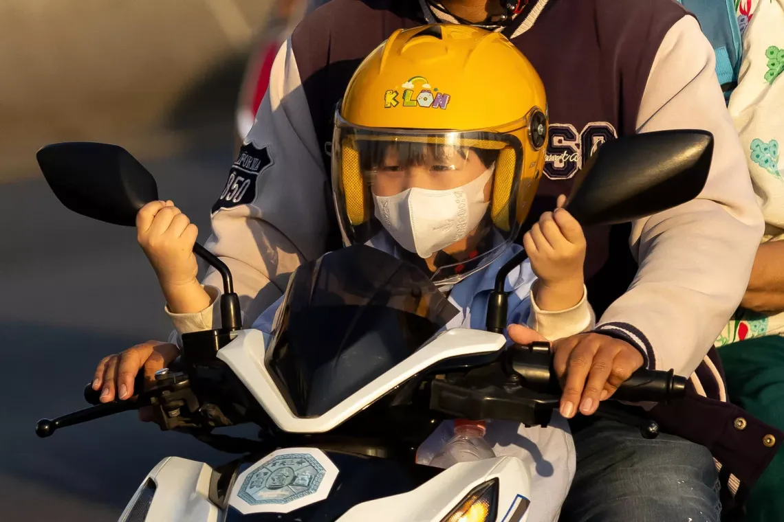 A schoolchild wearing a dust mask on a motorcycle, traveling in the evening when PM 2.5 levels in many areas exceeded the standard, starting to impact health.