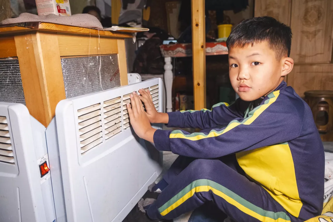 Bayan Erdene Munkh Ochir, 8, warming his hands on the CHIP inside his grandmother&rsquo;s ger in Ulaanbaatar&rsquo;s Bayanzurkh district. Unlike many others, his family ger is not heated by coal; instead, they use a UNICEF-provided CHIP (cooking, heating, and insulation package) device powered by electricity, significantly improving indoor air quality.