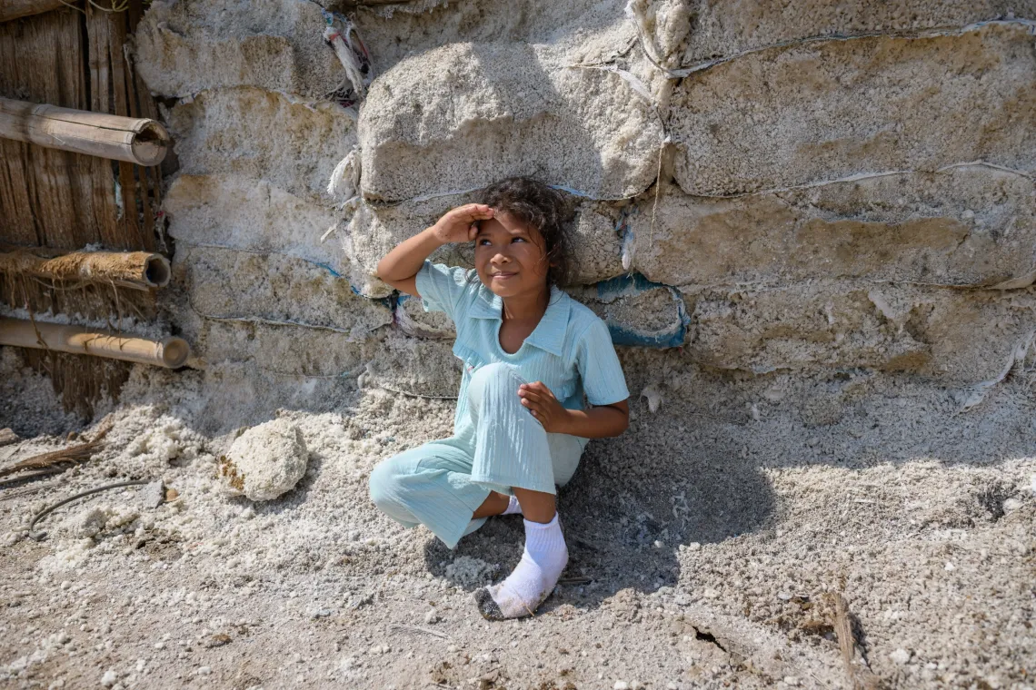 a girl sits in the sun by a rough, stone wall