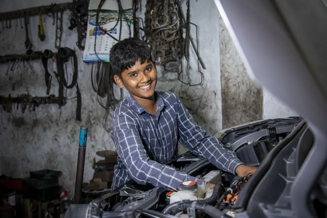 a teen boy smiles as he works on a car engine