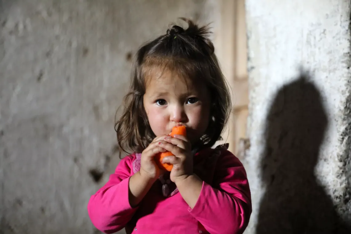 Azar (2) chews on a carrot that her mother Nikbakht picked from the crop field around their home.