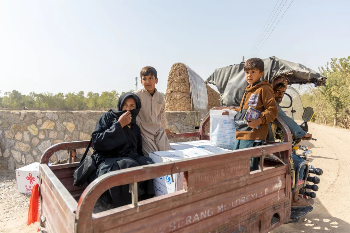 A father drives a cart with his family in the back as they return to their home village.