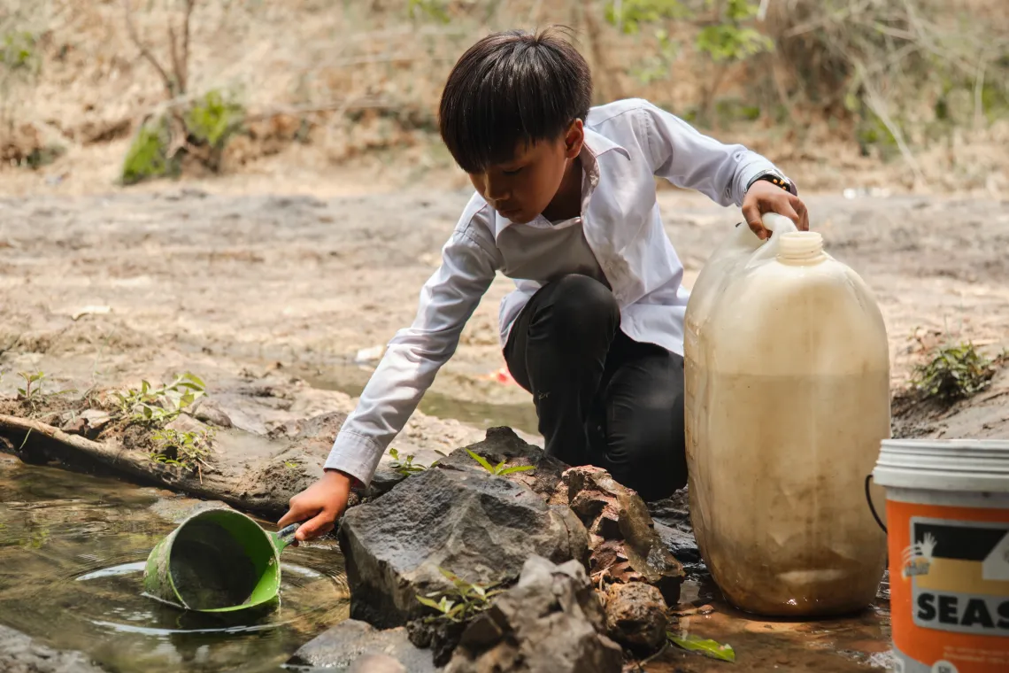 A boy scoops water from a stream into a jerry can