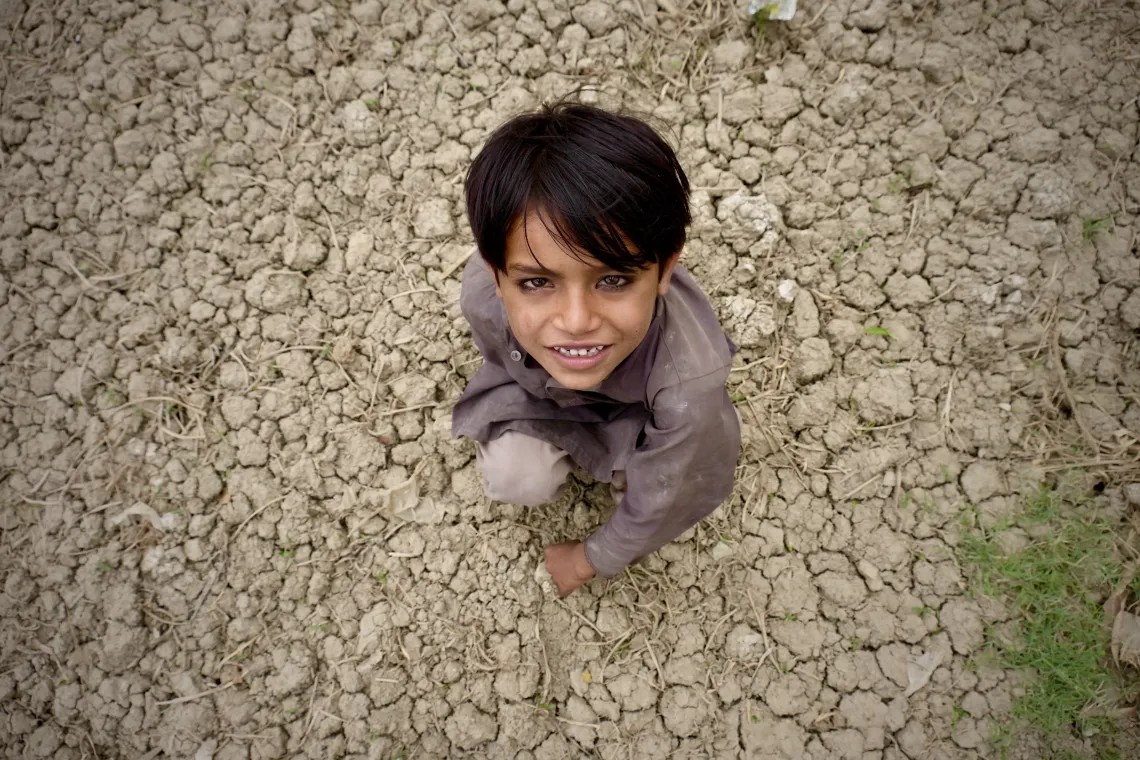 a boy standing on parched land looks up at the camera.