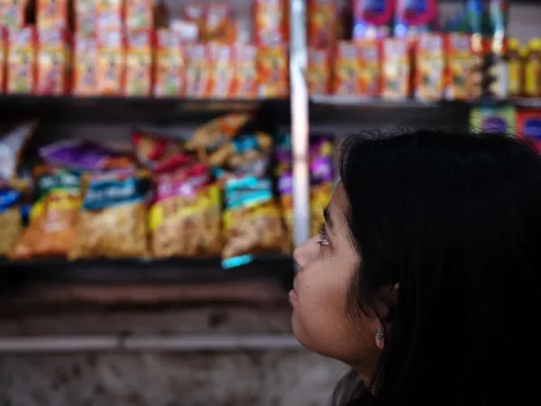 A girl looks toward shelves of snacks and drinks in a small neighborhood shop.